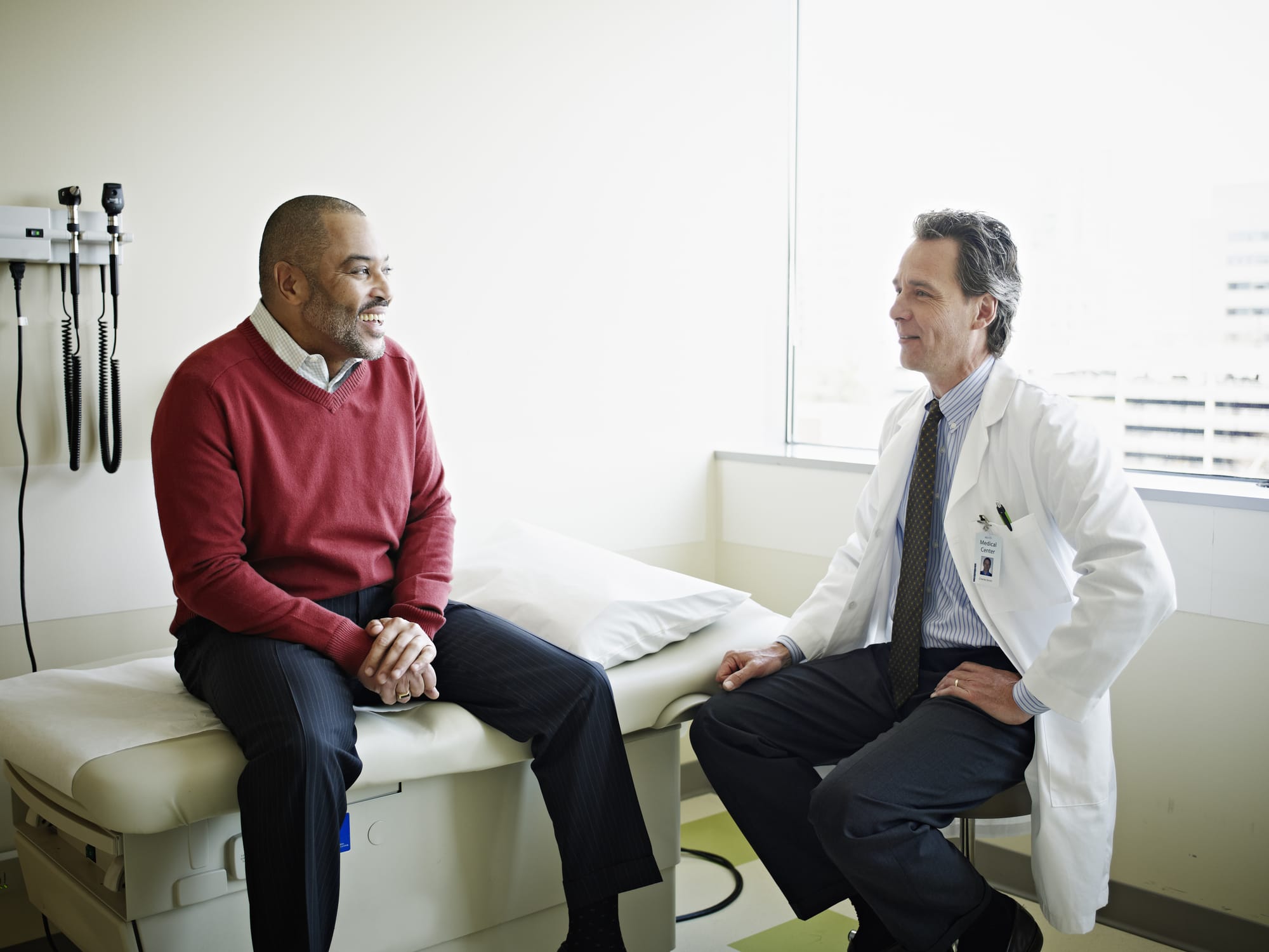 Older male patient sitting on exam table speaking with doctor