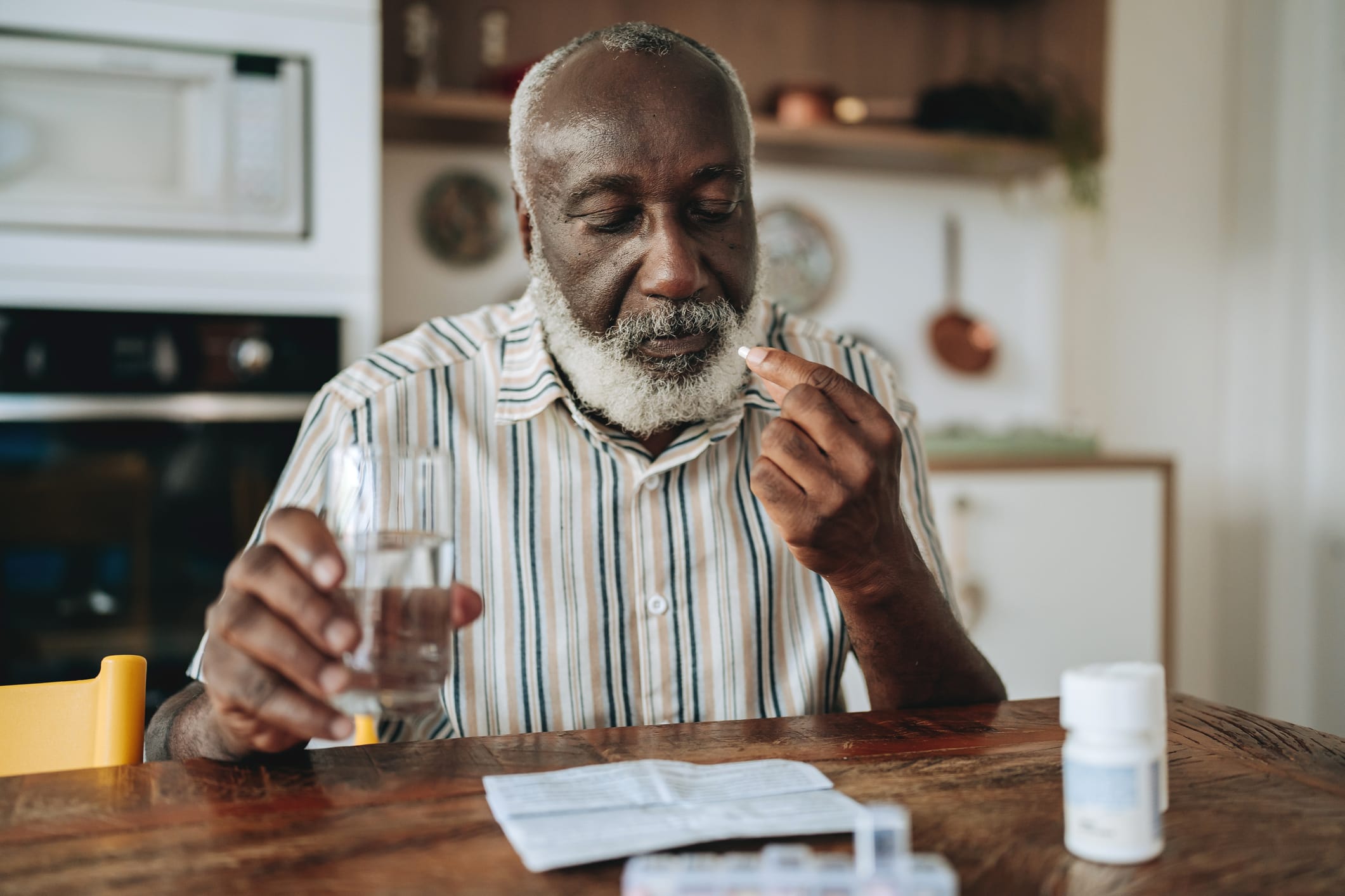 Photo of older Black man holding a glass of water while taking a pill