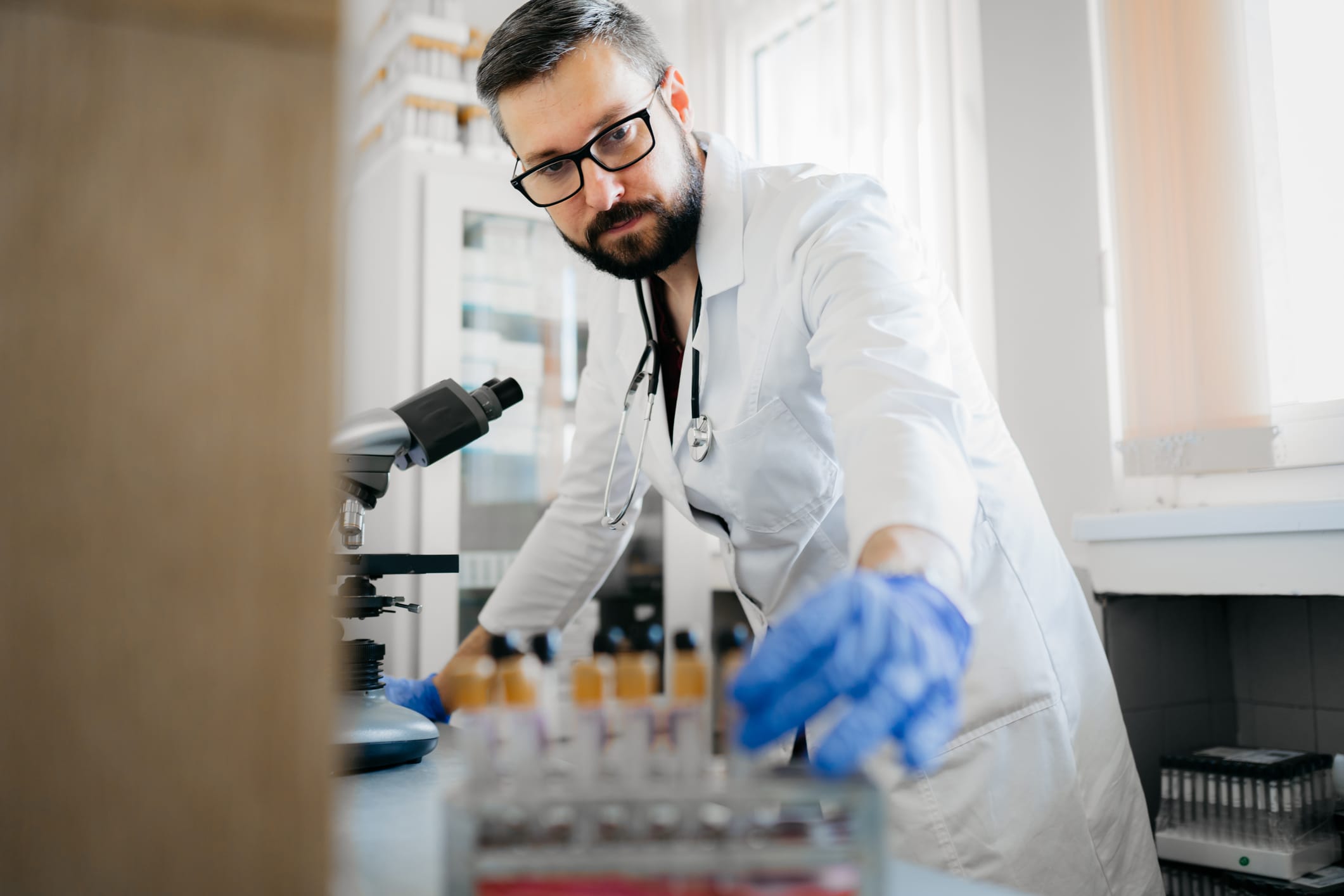 Researcher wearing a lab coat and protective gloves while using a telescope and checking blood cells