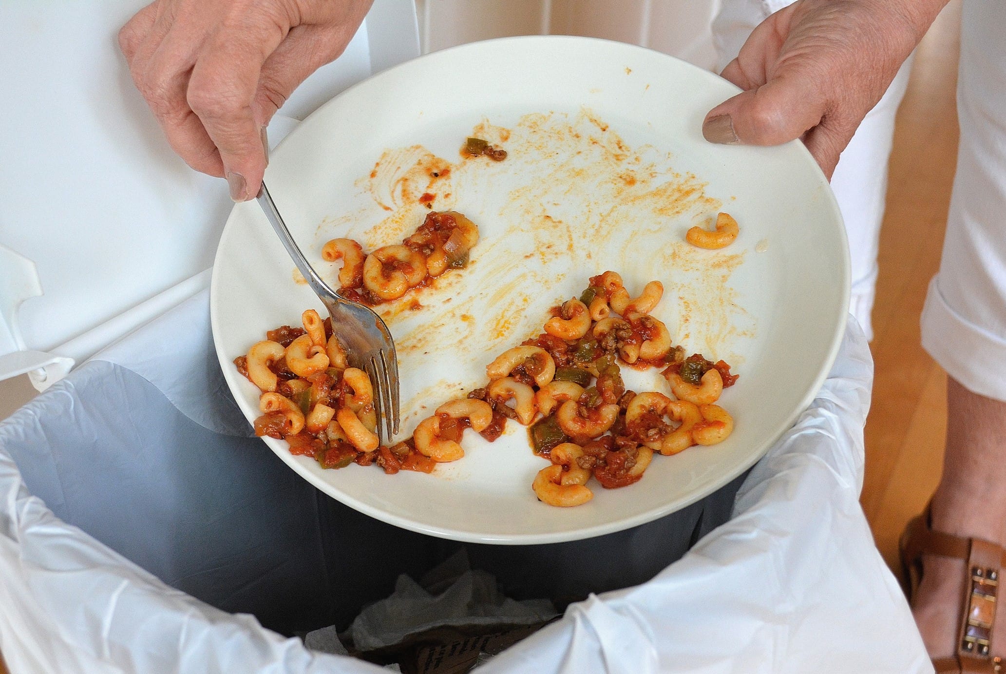Scraping pasta from plate to garbage