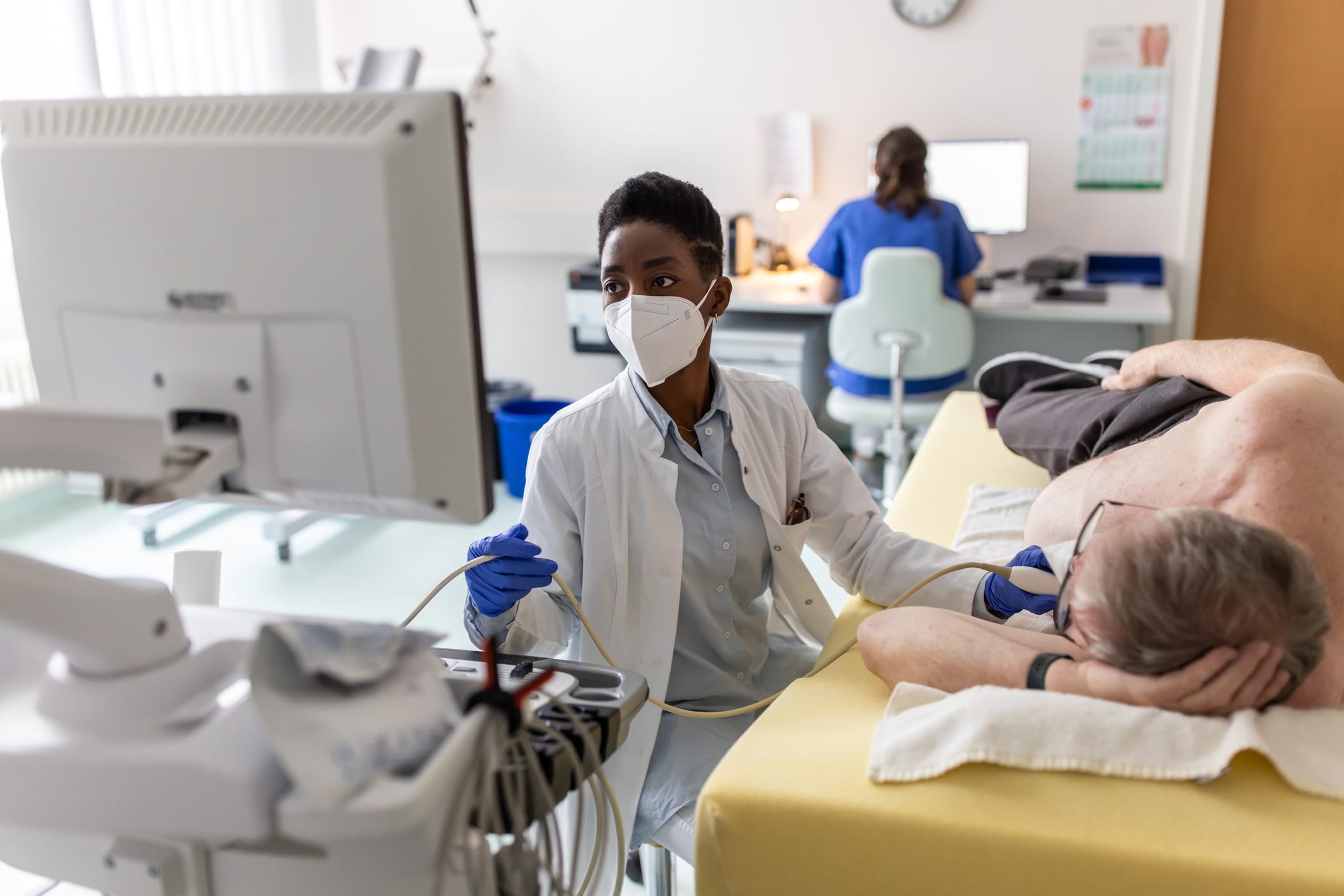 Female cardiologist looking at a computer screen while examining a male senior patient in the clinic.
